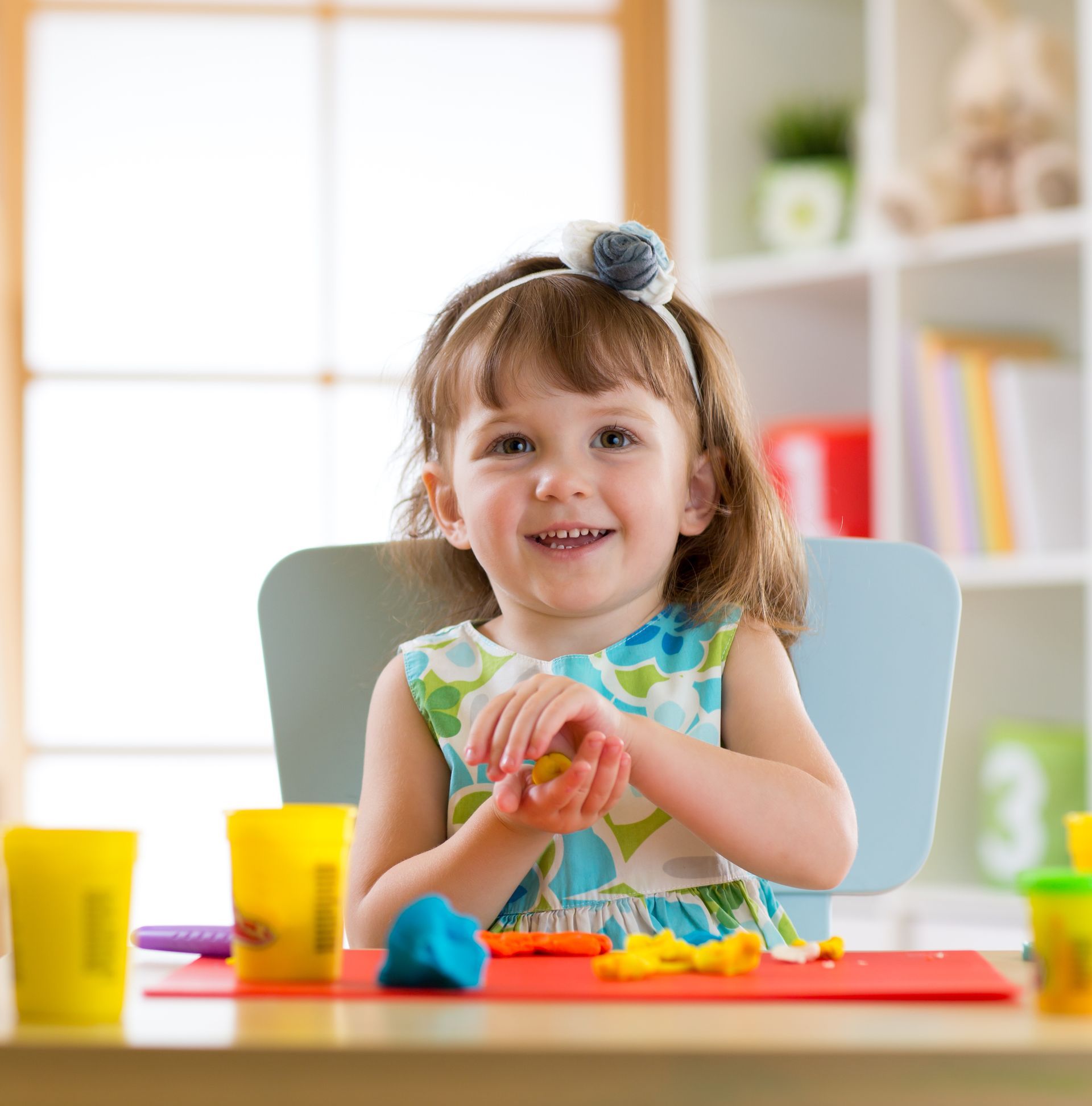 Smiling girl playing with plasticine or play dough at home.