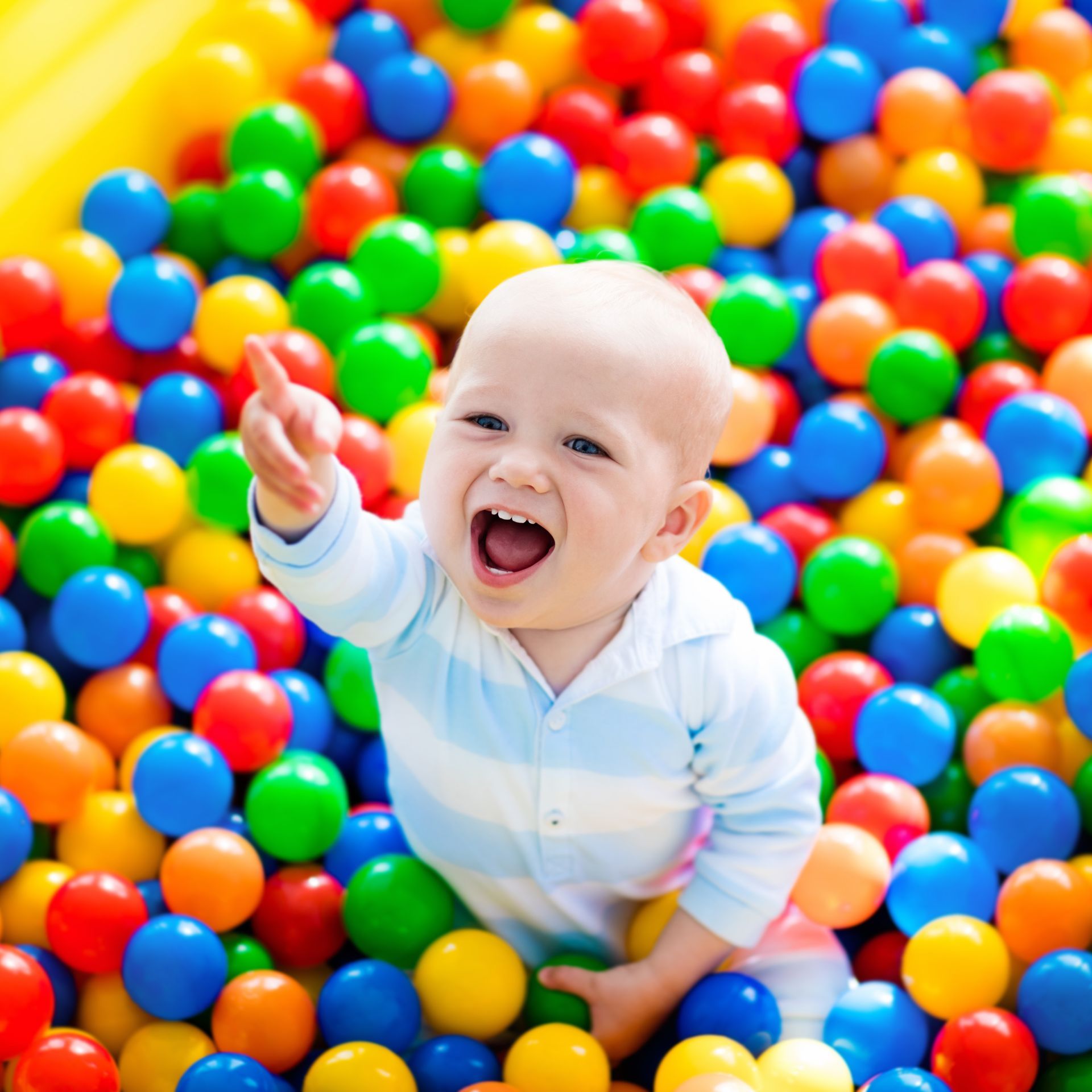 Happy laughing boy having fun in ball pit on birthday party in kids amusement park and indoor play center. Child playing with colorful balls in playground ball pool. Activity toys for little kid.