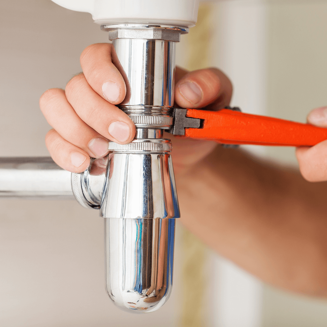 A person is fixing a sink pipe with a wrench.