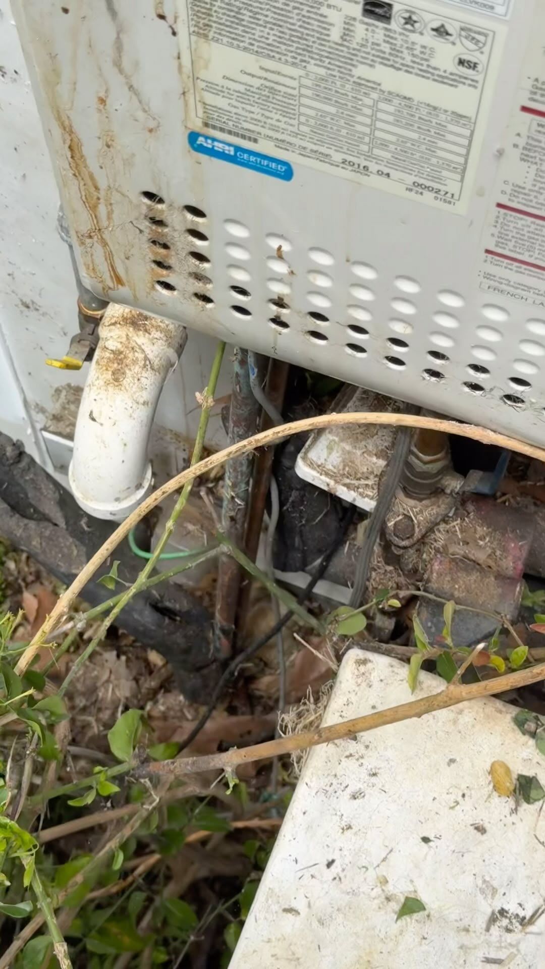 A dirty water heater is sitting in the grass next to a white box.