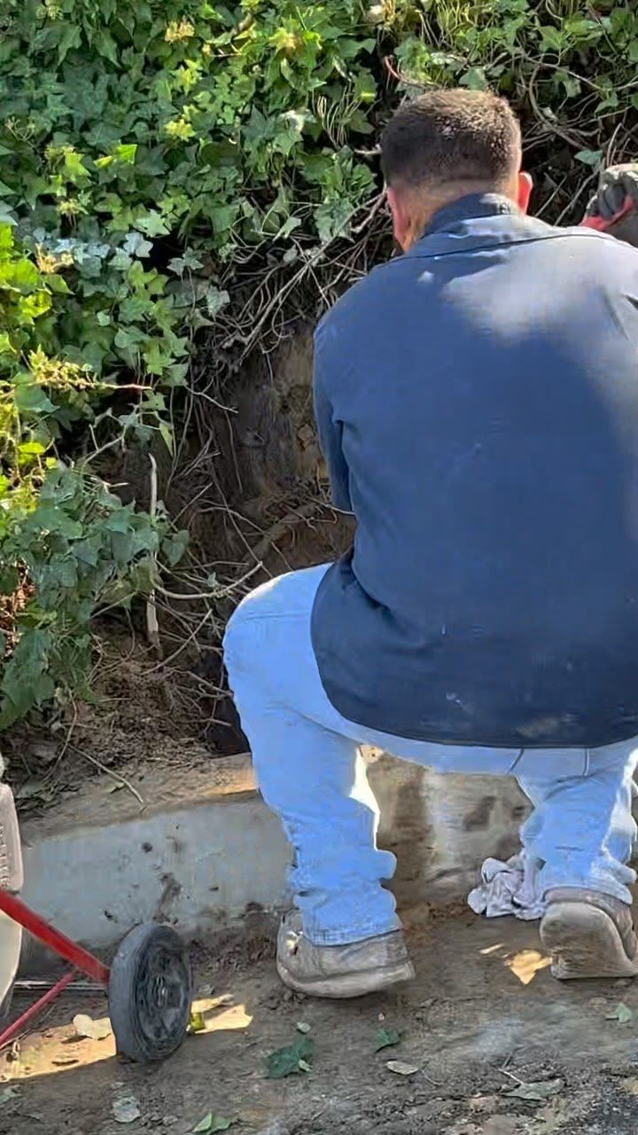 A man is sitting on the ground next to a wheelbarrow.