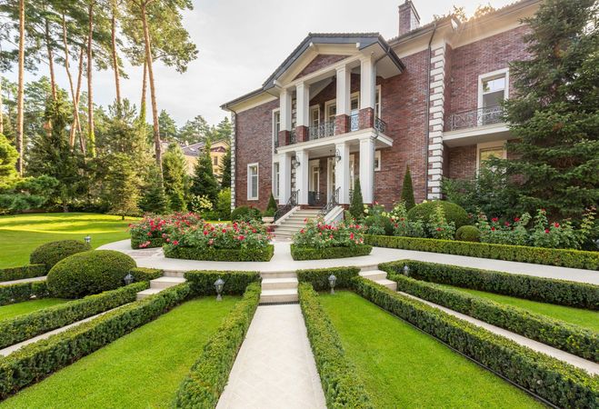 A large brick house with a lush green garden in front of it.