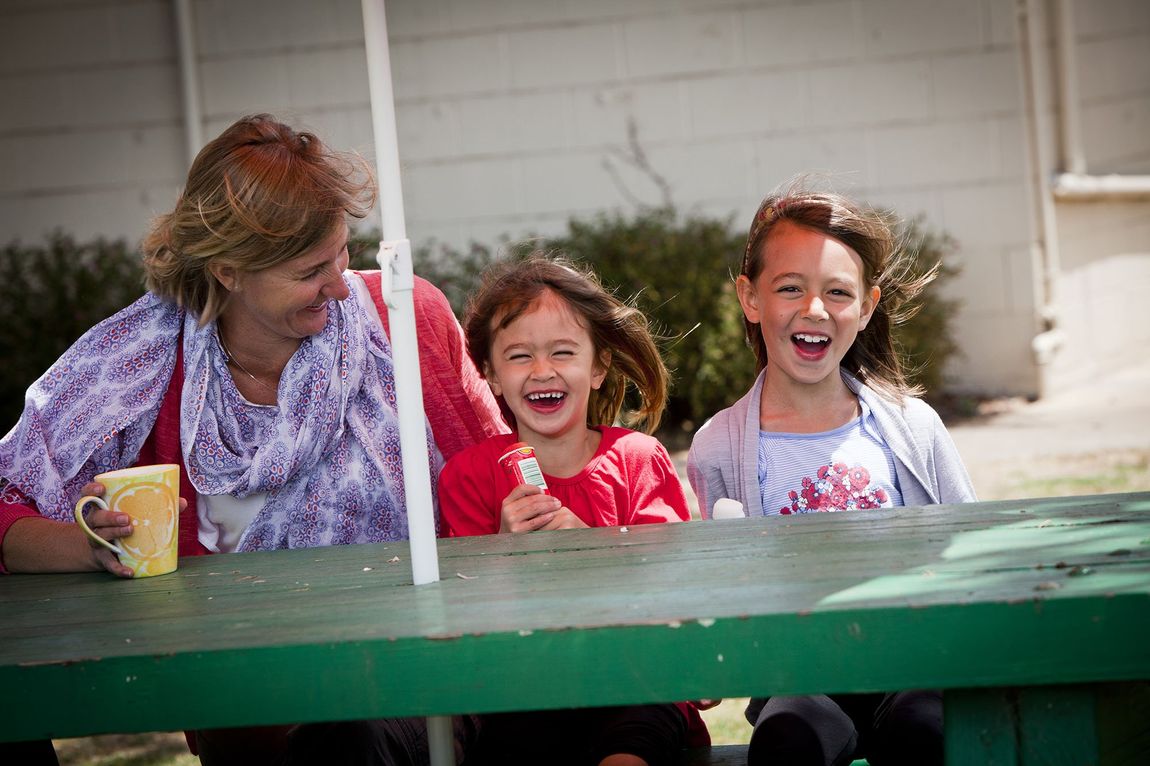 A mother with her two daughters at Gum Tree Caravan Park, sitting on a bench and enjoying drinks and icy poles
