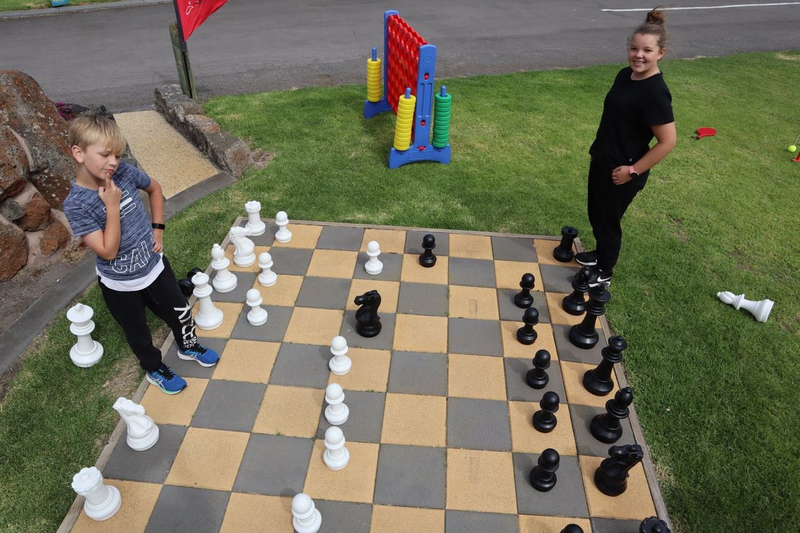 Girl and boy ponder their next moves as they play with a giant chess set at Gum Tree Caravan Park