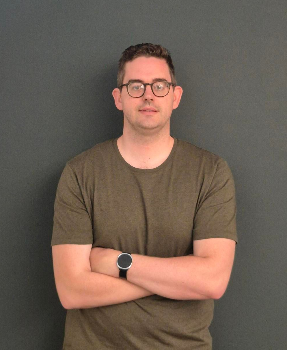 Man in a warehouse, using a tablet, surrounded by boxes on shelves.