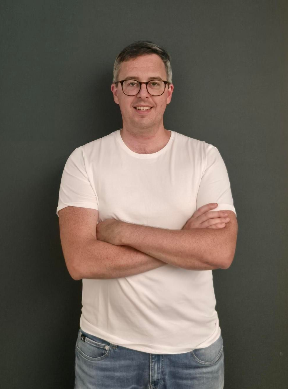 Man in blue shirt smiles in office setting, natural light.