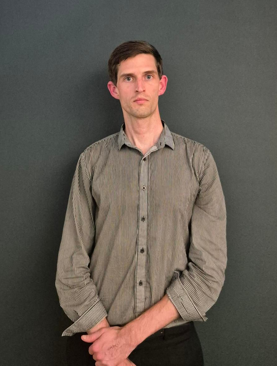 Man in a warehouse, using a tablet, surrounded by boxes on shelves.