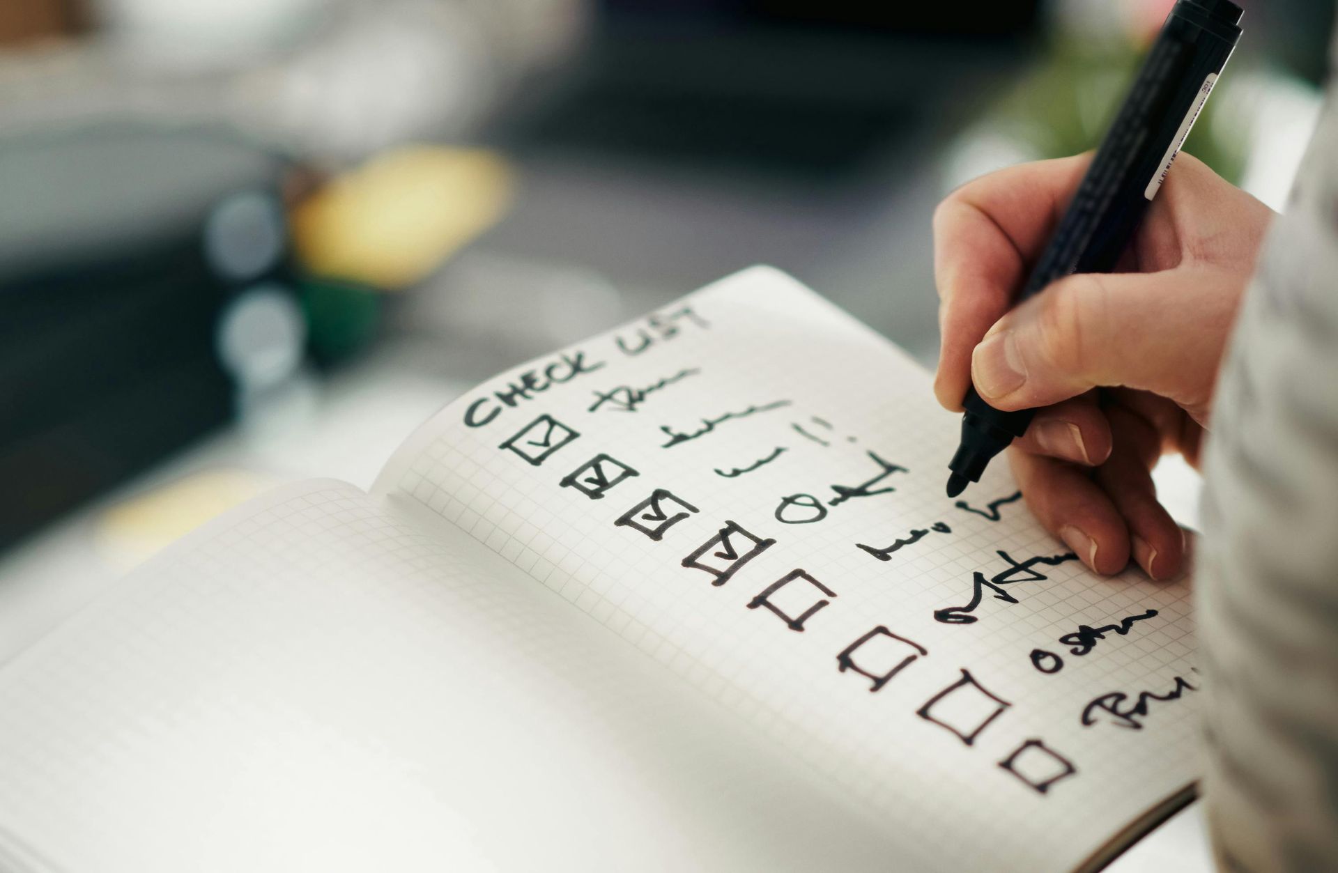 A person uses a black marker to check items off a handwritten checklist in a notebook.