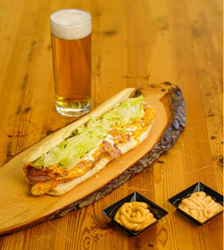 Panino con lattuga, birra e salse su un tagliere di legno.