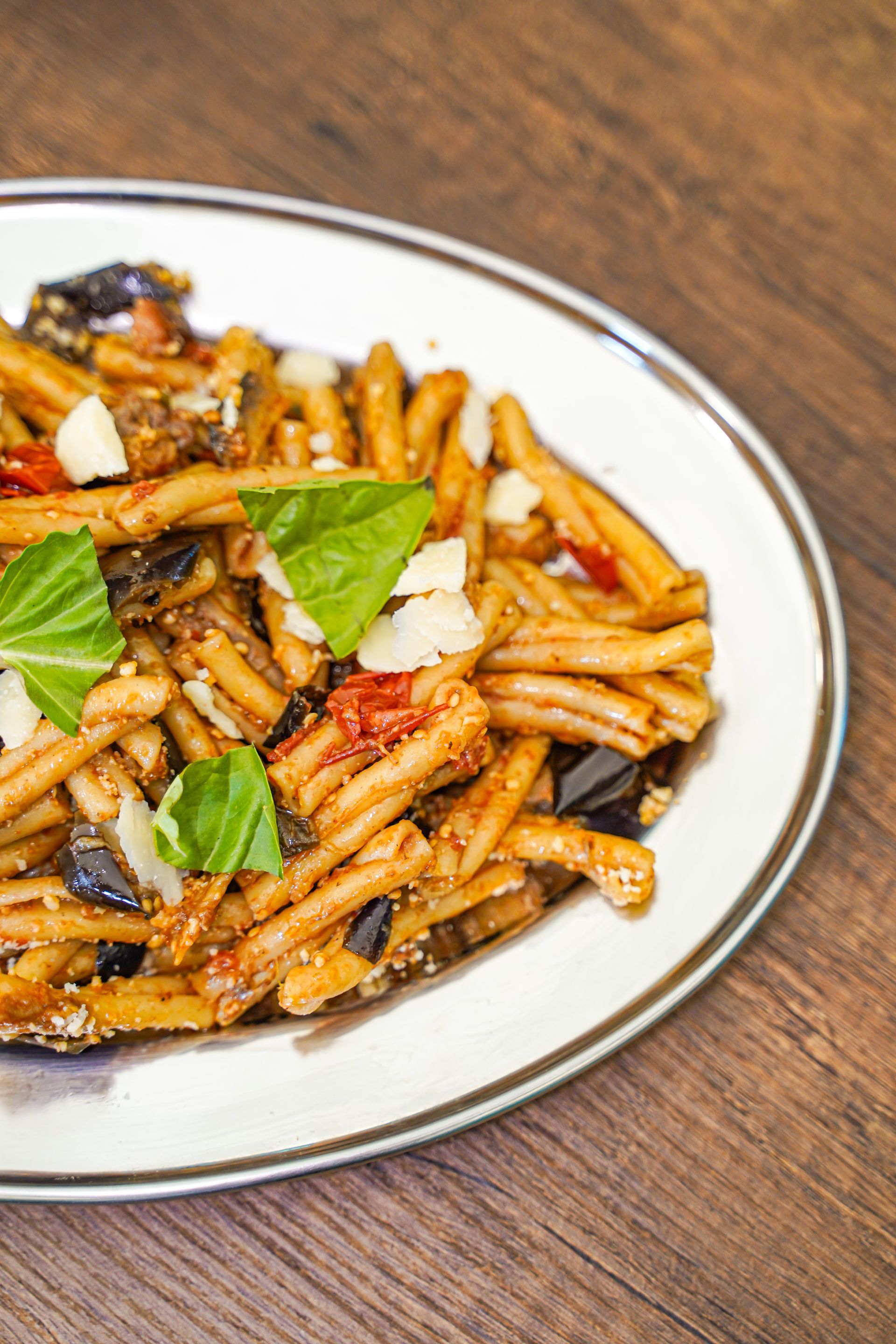 Pasta con melanzane, pomodori, basilico e parmigiano su un piatto d'argento.