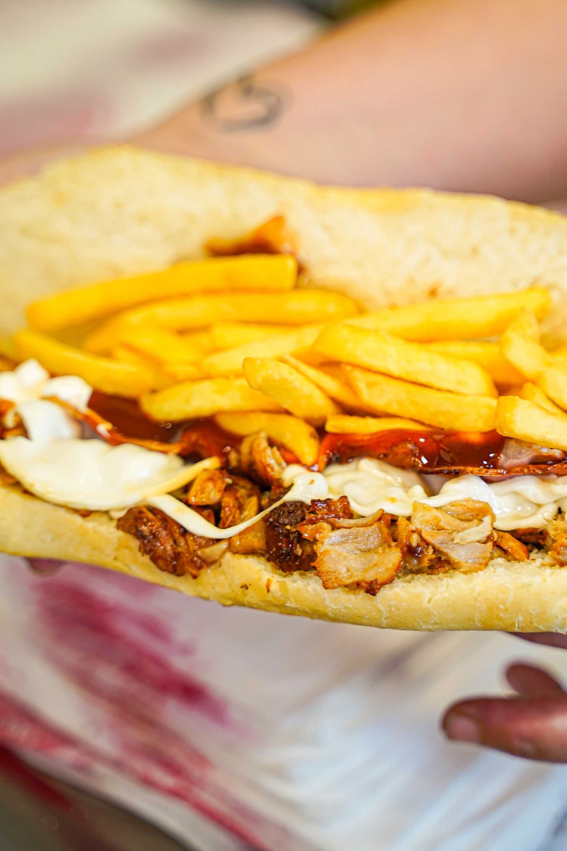 Grande panino ripieno di patatine fritte, carne e salsa, tenuto in mano da una persona.