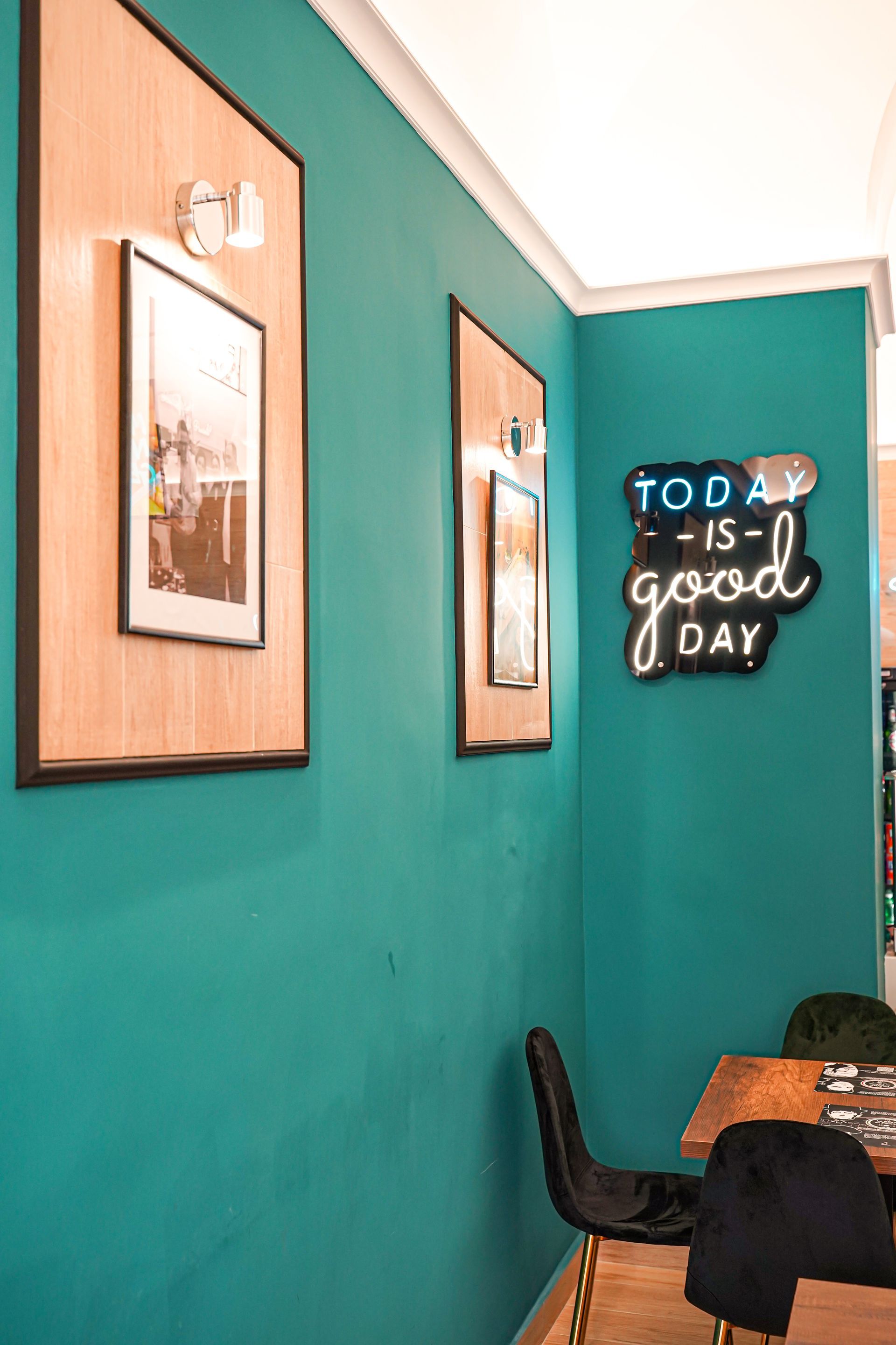 Parete color verde acqua con opere d'arte incorniciate e scritta al neon