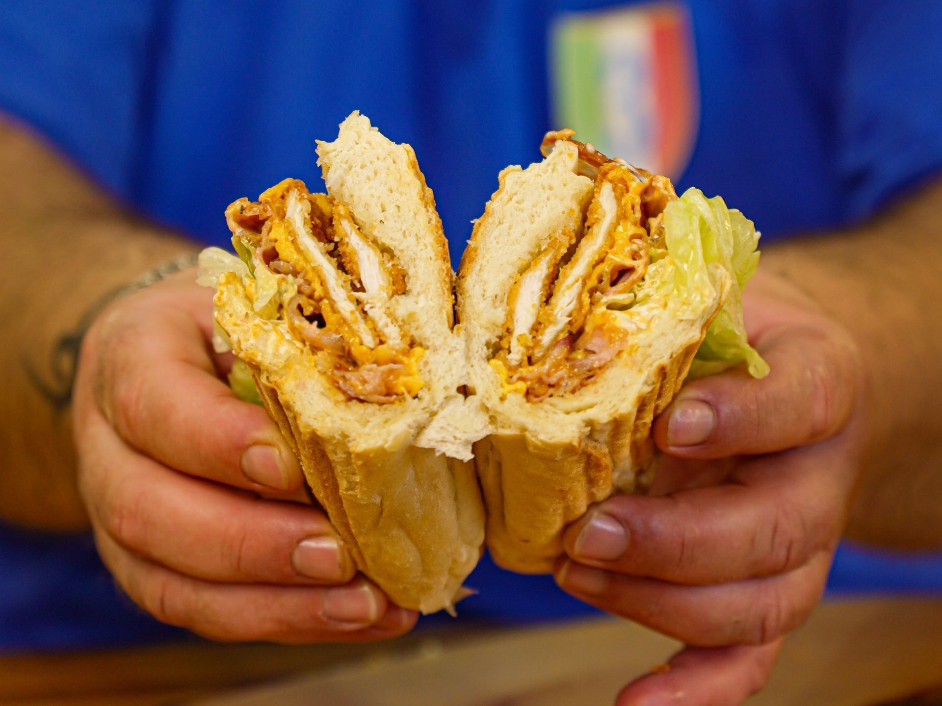 Persona che tiene in mano un grande panino tagliato a metà; sono visibili pollo, formaggio e lattuga.