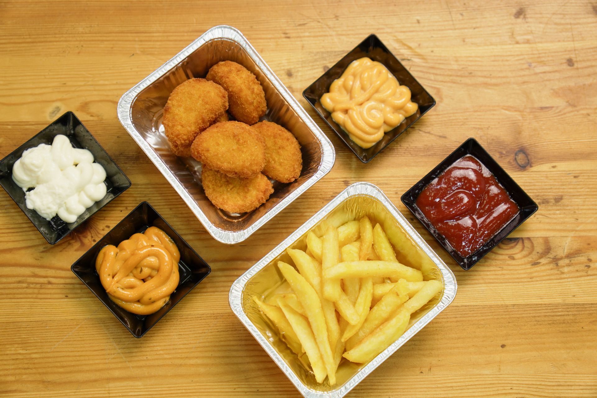 Nuggets di pollo, patatine fritte e salse in contenitori da asporto su un tavolo di legno.
