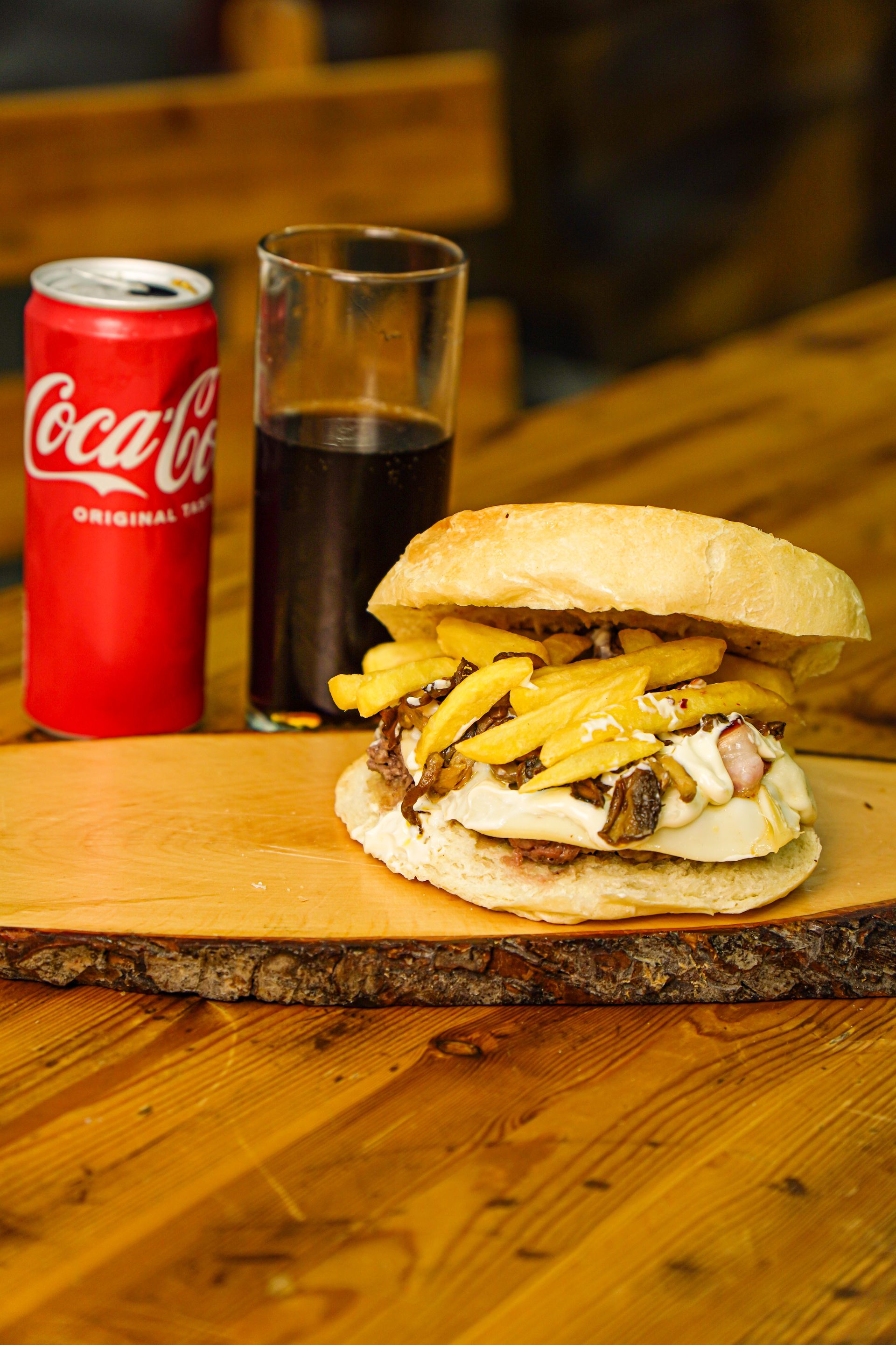 Hamburger con patatine fritte, bibita e una lattina di Coca-Cola su un tagliere di legno.
