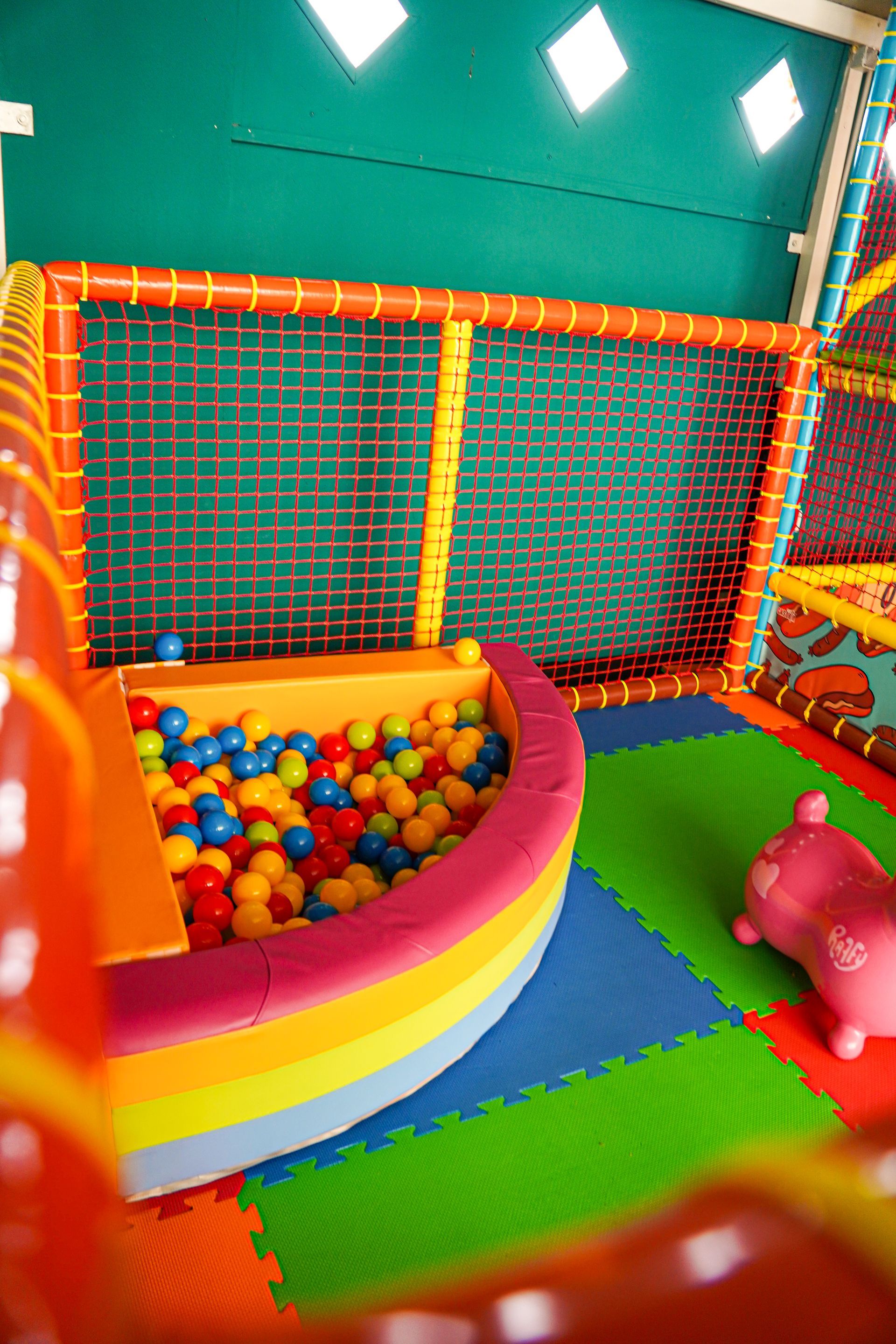 Piscina di palline colorate con barca color arcobaleno, all'interno di un'area giochi per bambini con pavimenti imbottiti.
