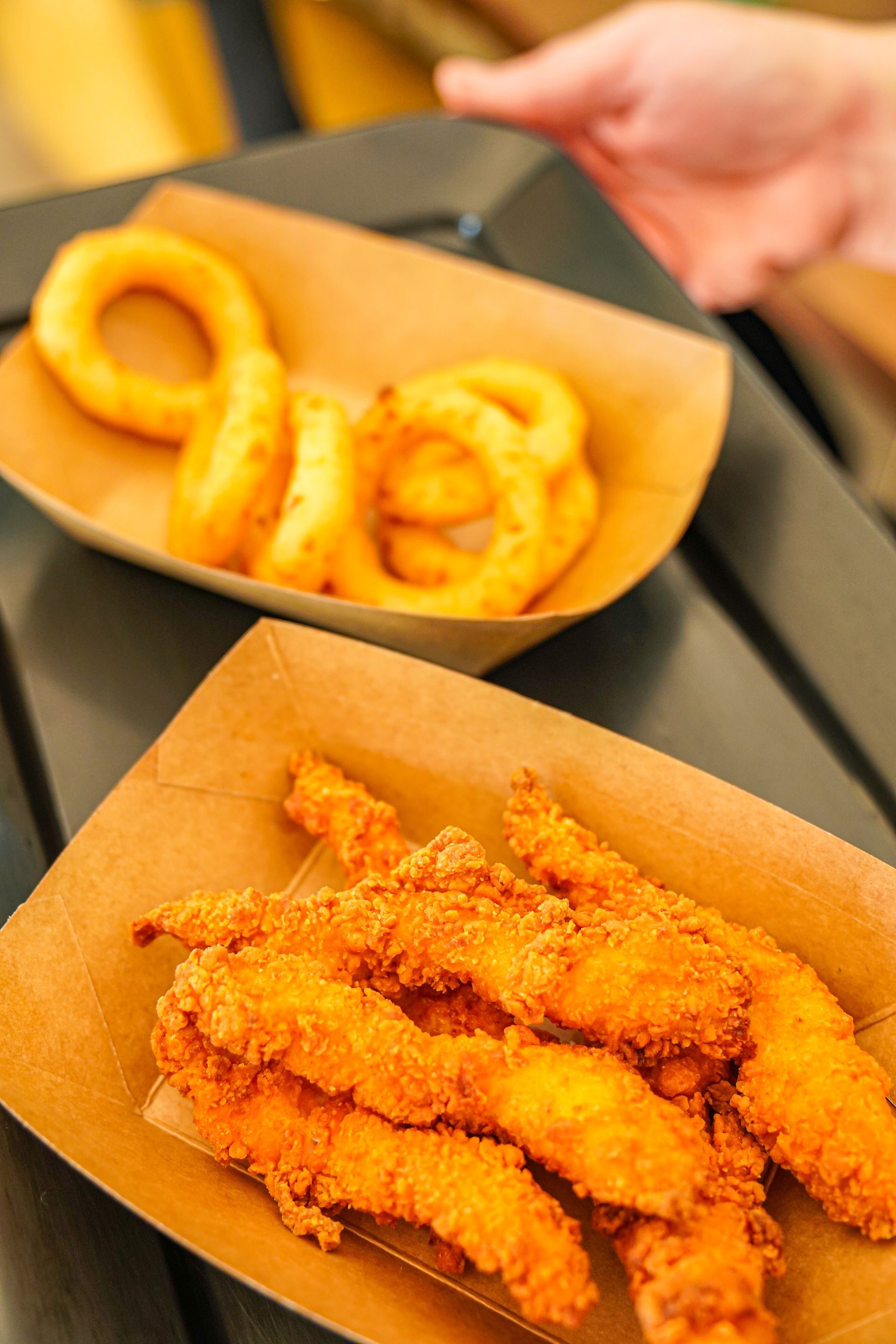 Striscioline di pollo fritte e anelli di cipolla su vassoi di carta. Mano che tiene il vassoio.