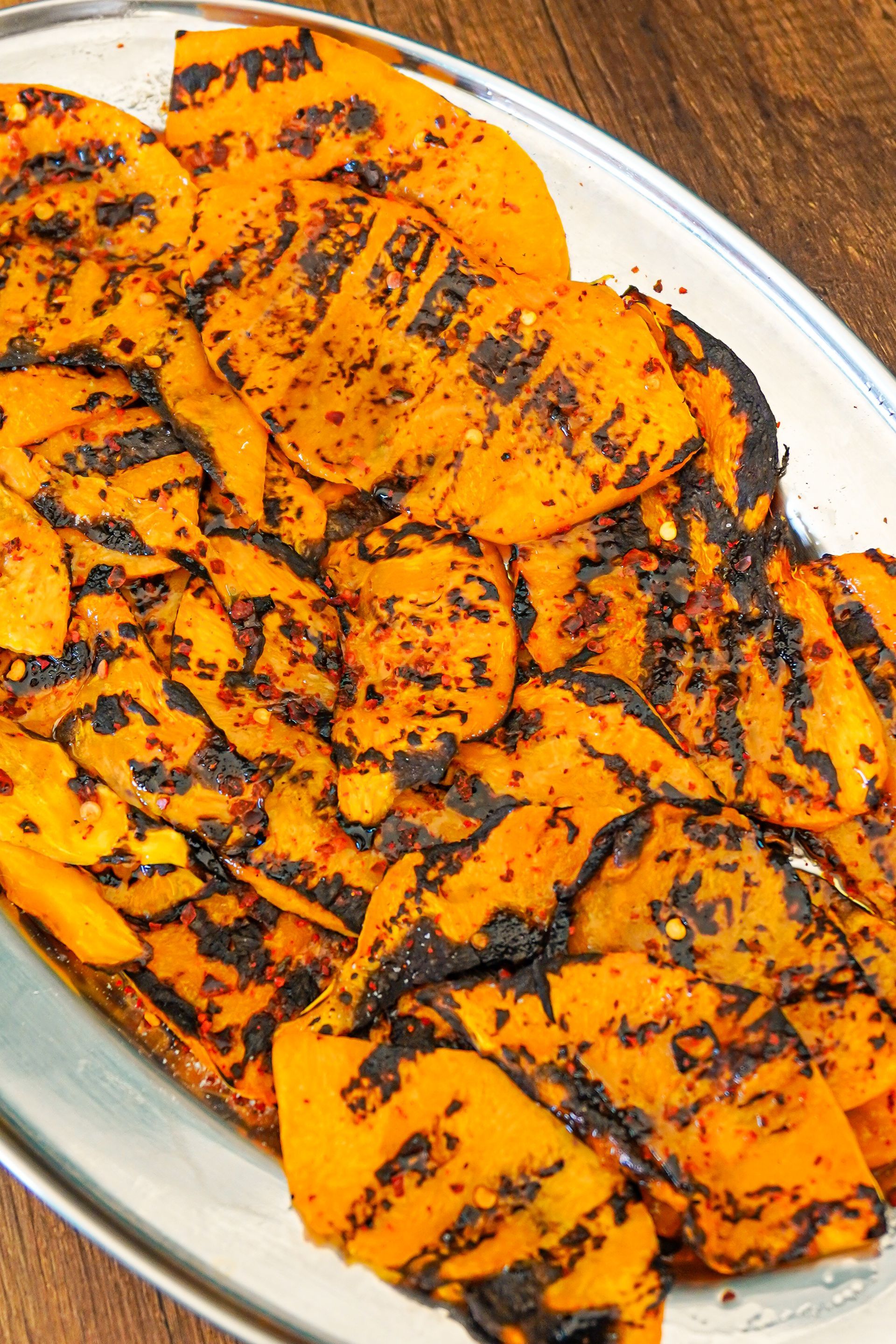Fette di zucca grigliate su un piatto d'argento, con i segni scuri della griglia e del condimento.
