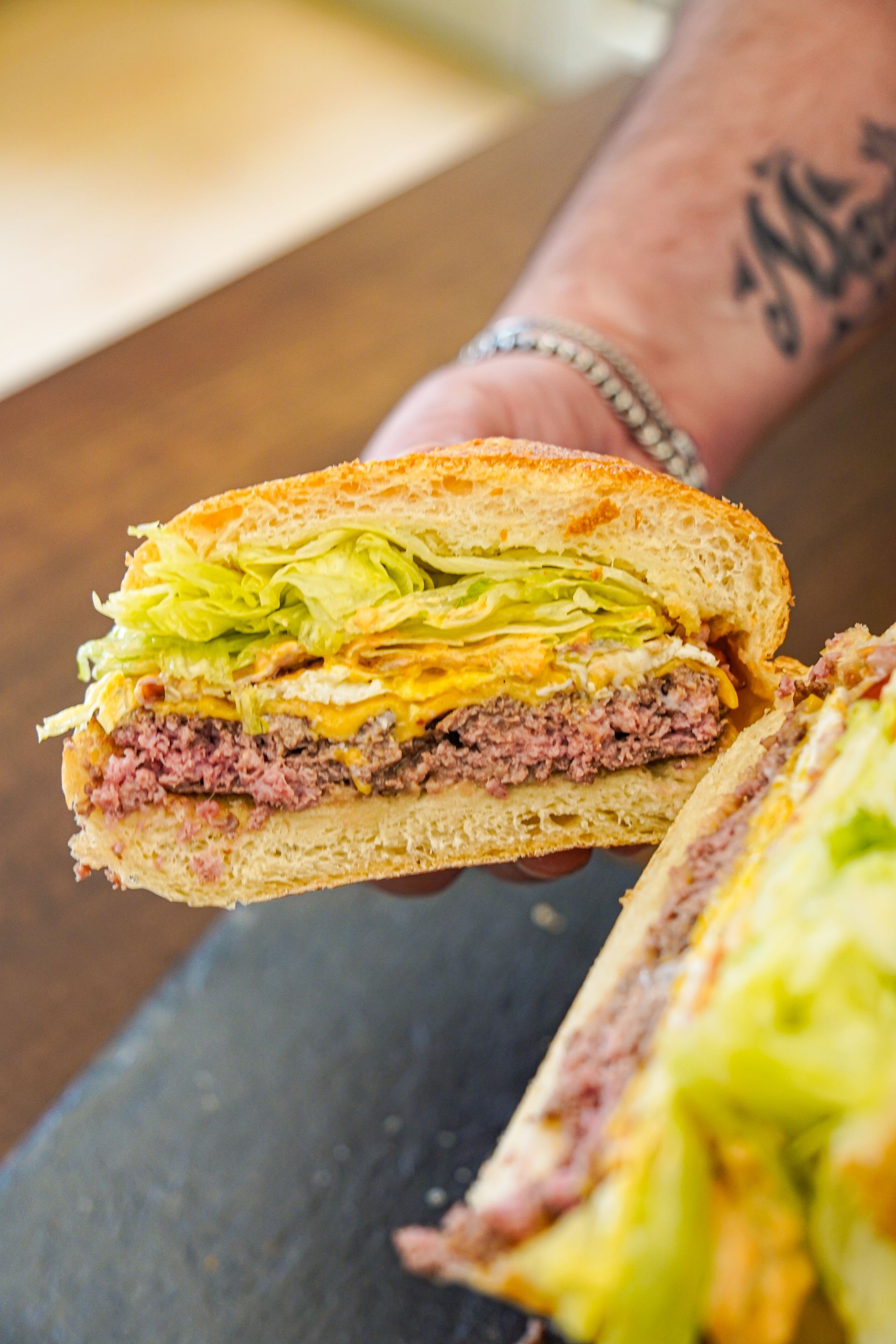 Sezione trasversale di un hamburger tenuto in mano. Mostra un hamburger, formaggio e lattuga in un panino tostato.