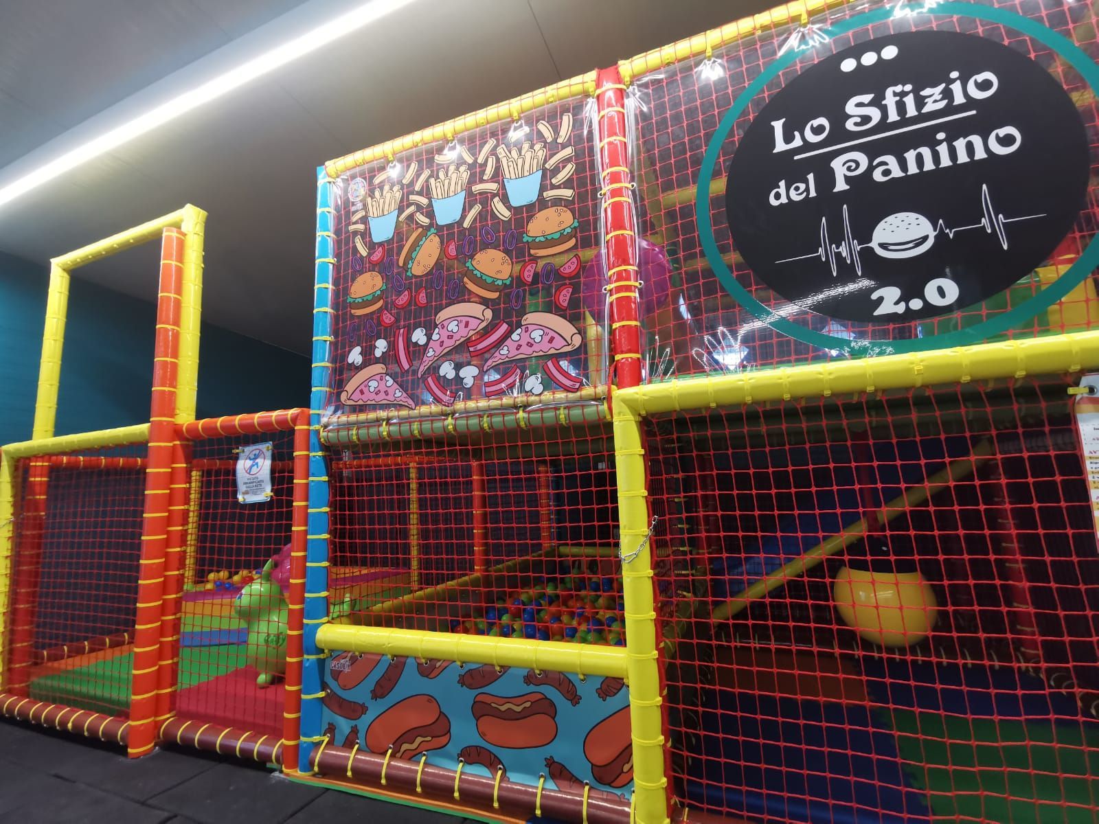 Area giochi con reti colorate, piscina di palline e decorazioni a tema culinario.