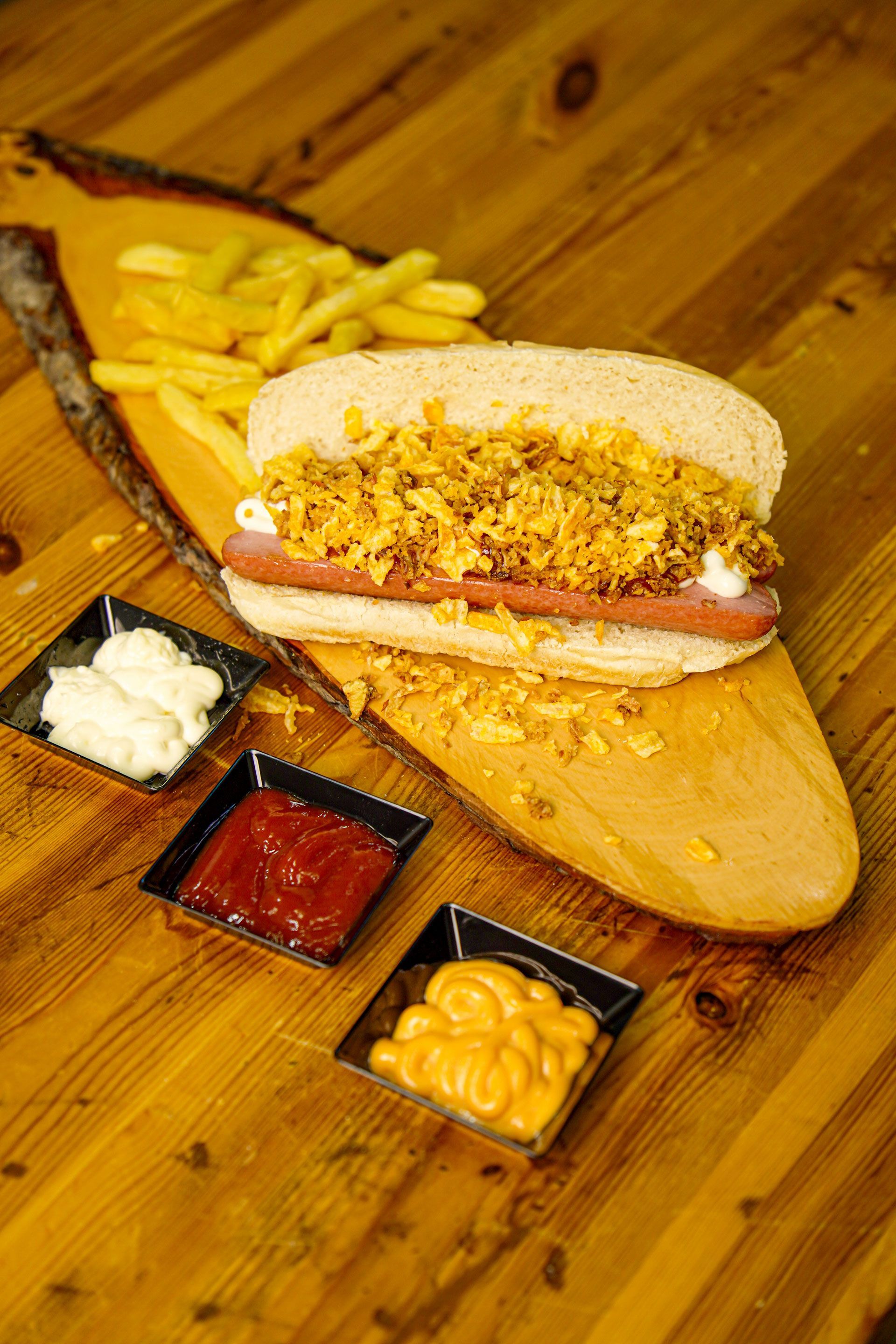 Hot dog su un vassoio di legno con patatine fritte e salse.