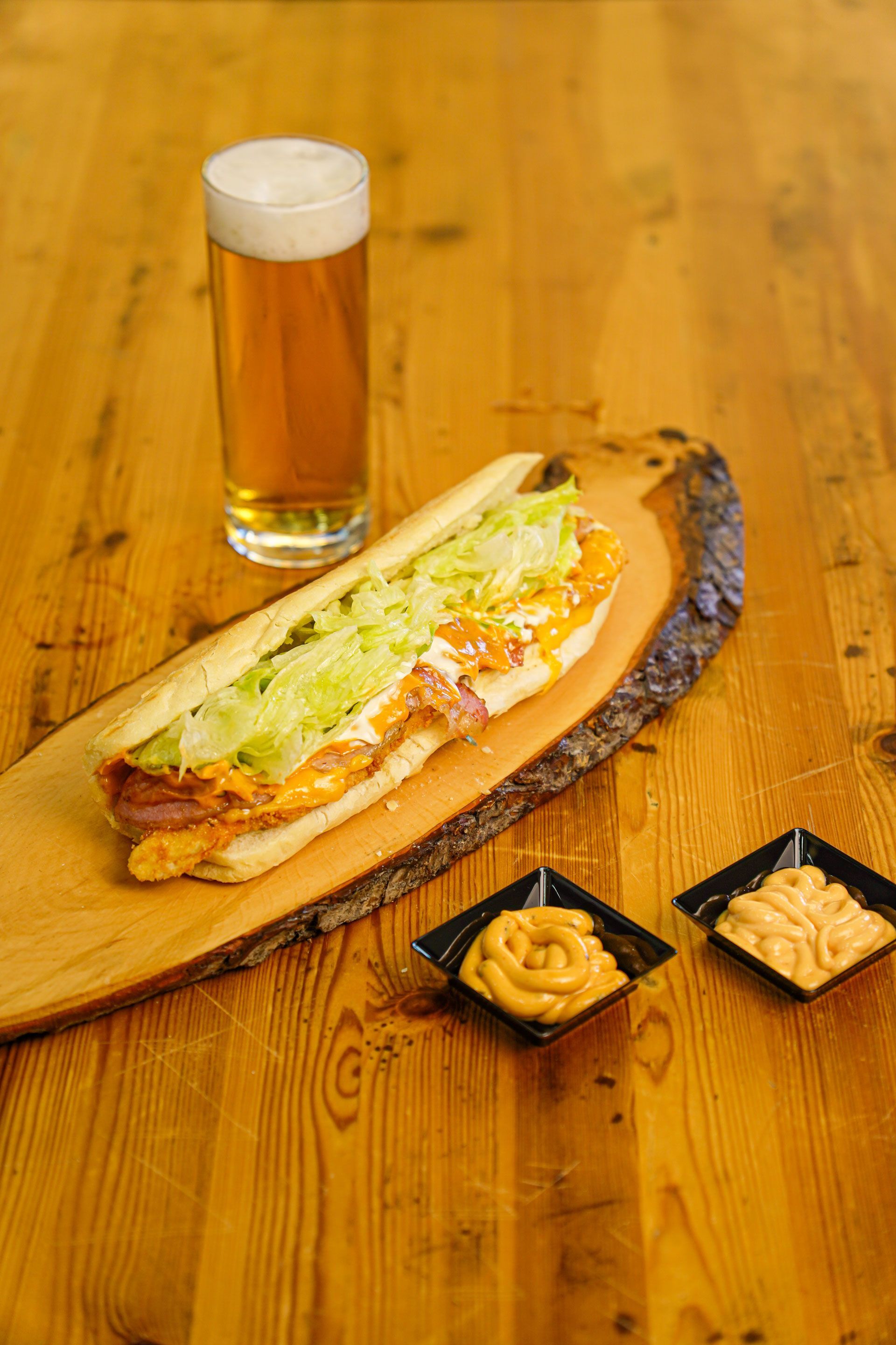 Panino con lattuga, birra e salse su un tagliere di legno, appoggiato su un tavolo di legno.
