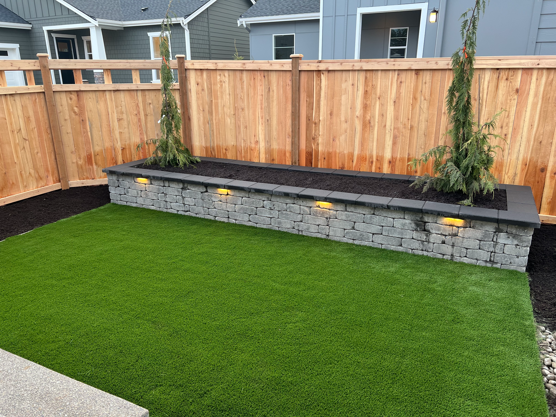 A wooden fence surrounds a lush green lawn in a backyard.