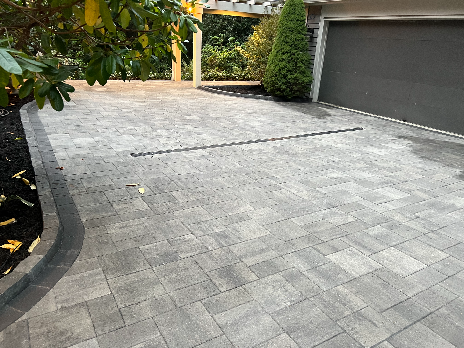 A brick driveway leading to a garage with a tree in the background.