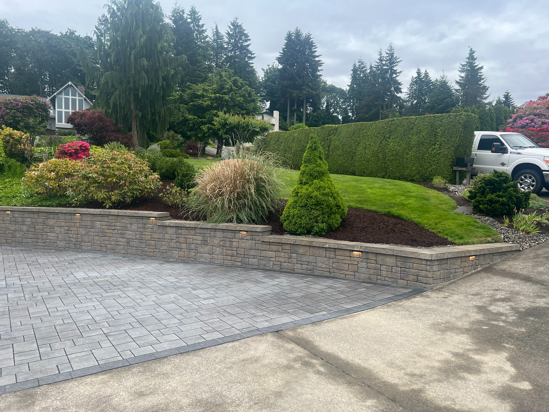 A white truck is parked in a driveway next to a stone wall.