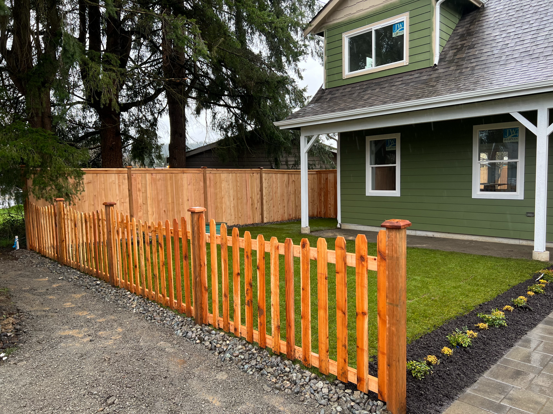 A green house with a wooden picket fence in front of it.