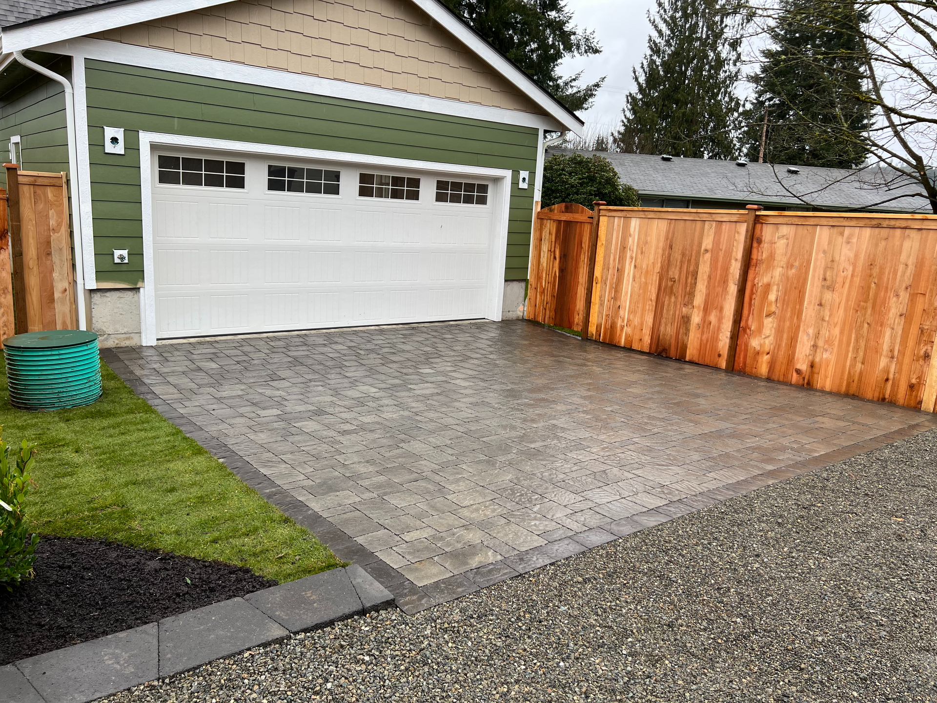 A garage with a wooden fence around it and a driveway leading to it.