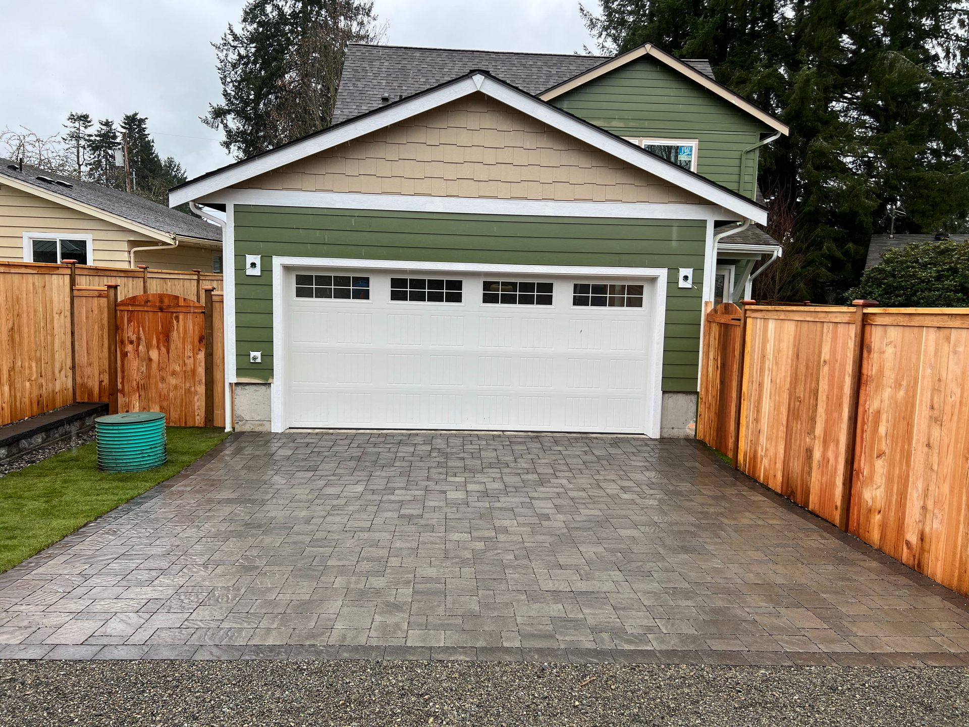 A green house with a white garage door and a wooden fence.