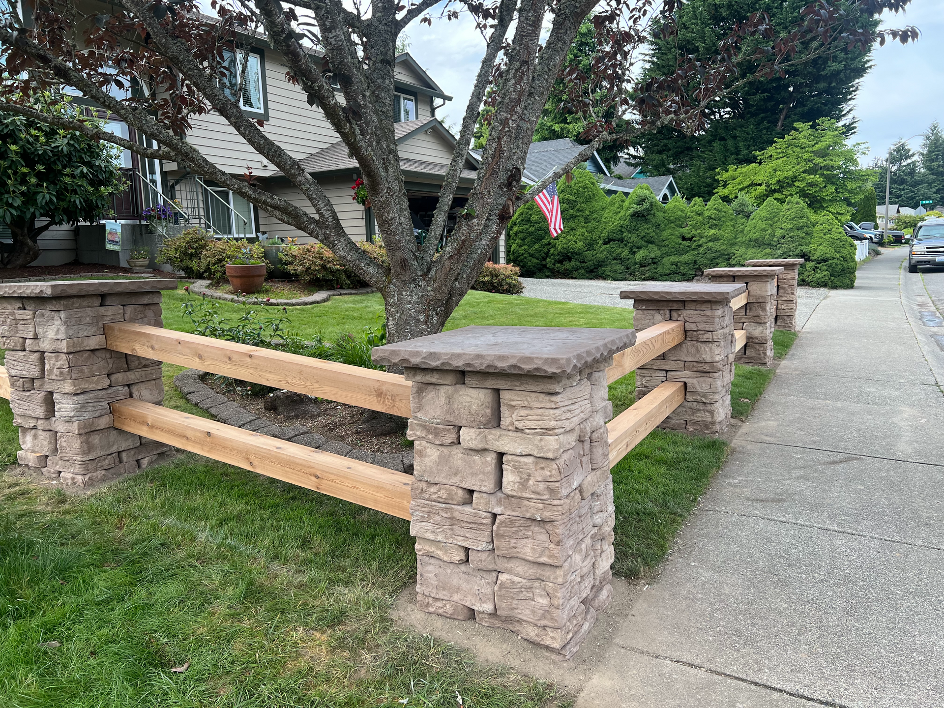 A wooden fence is surrounded by brick pillars in front of a house.