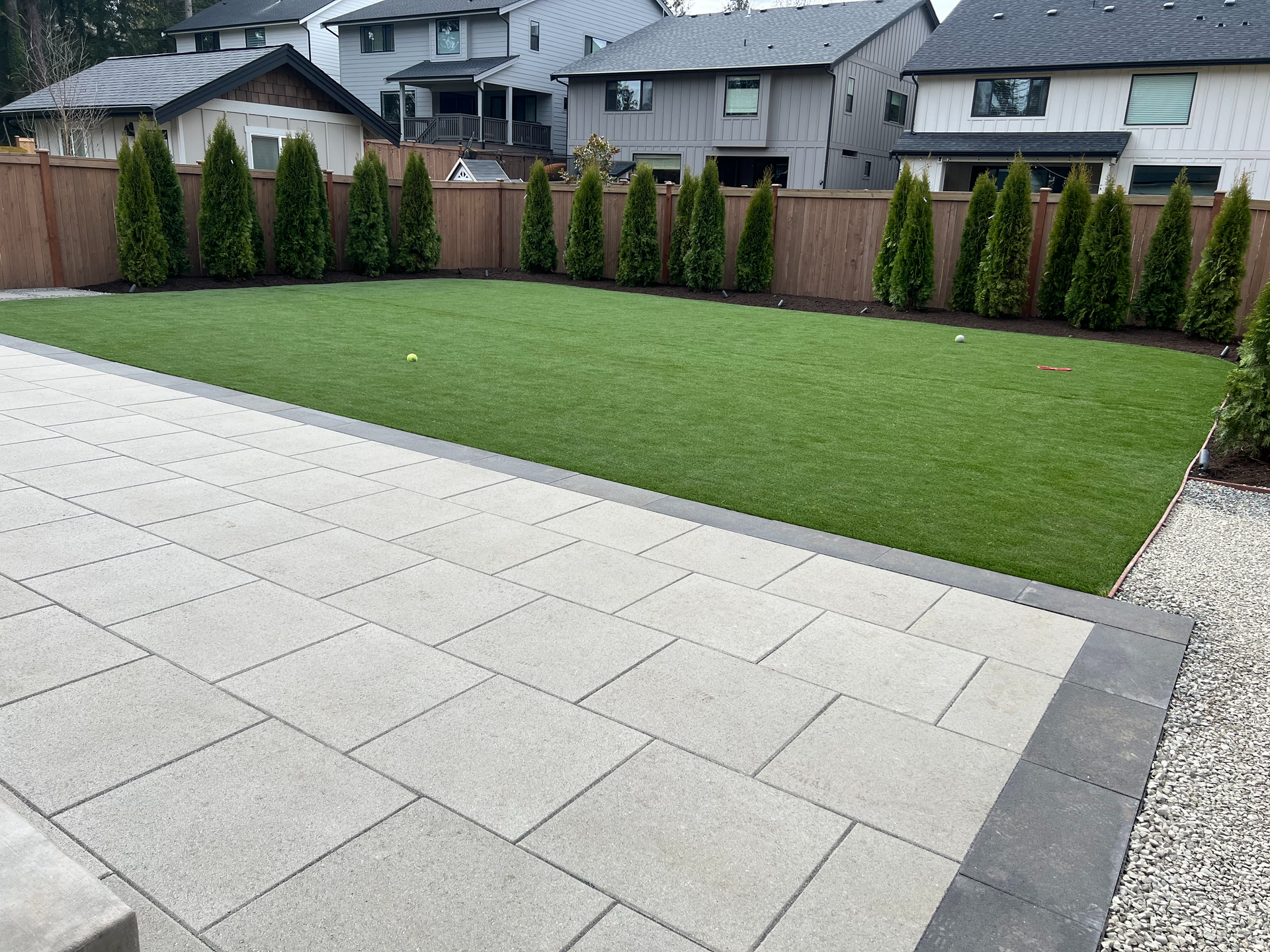 A backyard with a patio , grass , trees and a fence.