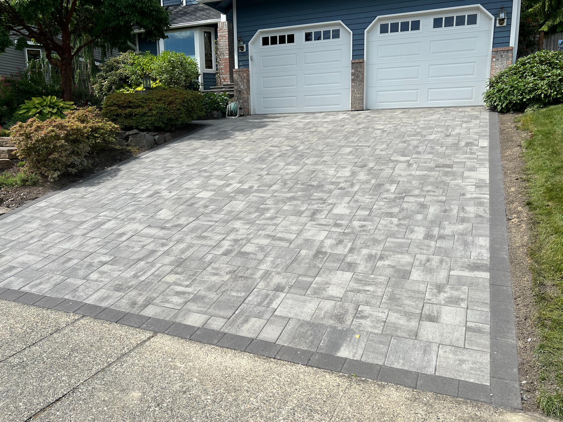 A brick driveway leading to a house with two garage doors.