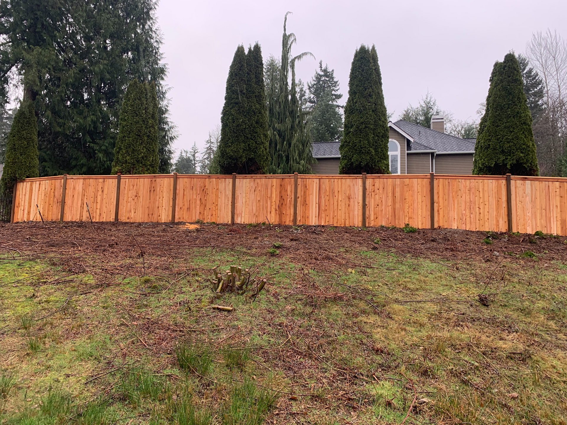 A wooden fence surrounds a grassy field in front of a house.