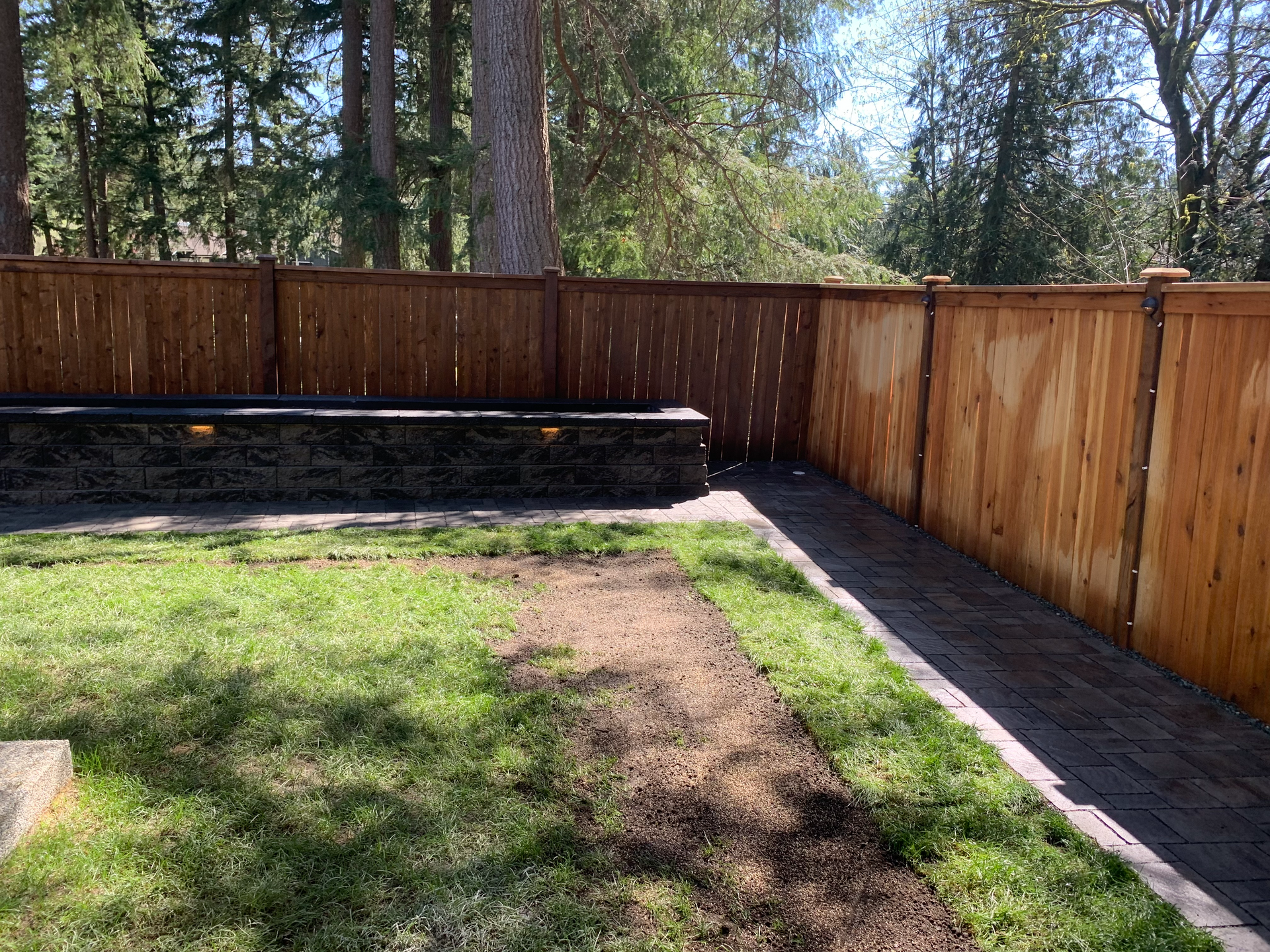 A wooden fence surrounds a lush green yard with trees in the background.