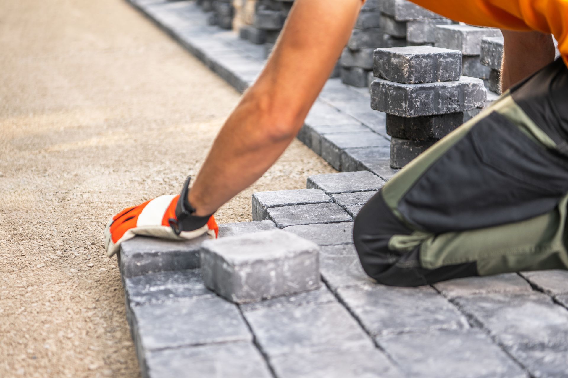 A man is kneeling down and laying pavers on the ground.