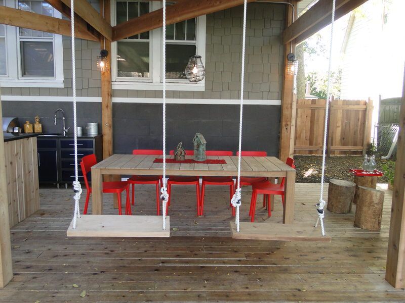 A wooden patio with a table and chairs and two swings