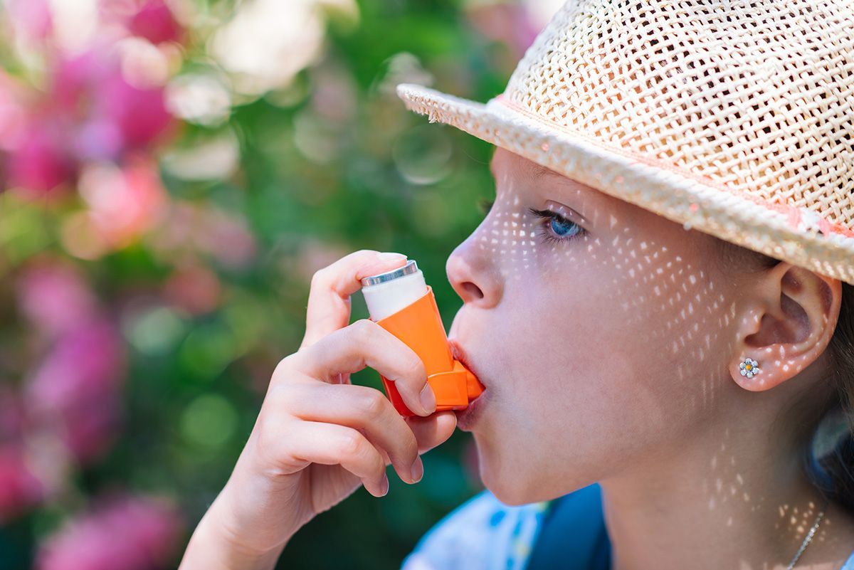 A child in a sun hat is outside using an inhaler.