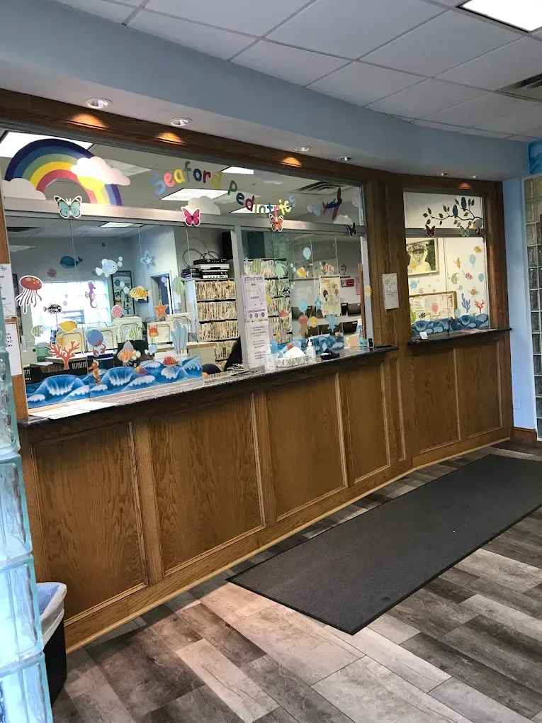 Reception desk with wood paneling, rainbow decor, and a waiting area in a pediatric office.