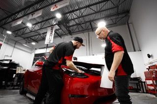 Deux hommes travaillent sur une voiture rouge dans un garage.