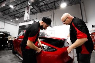 Deux hommes travaillent sur une voiture rouge dans un garage.