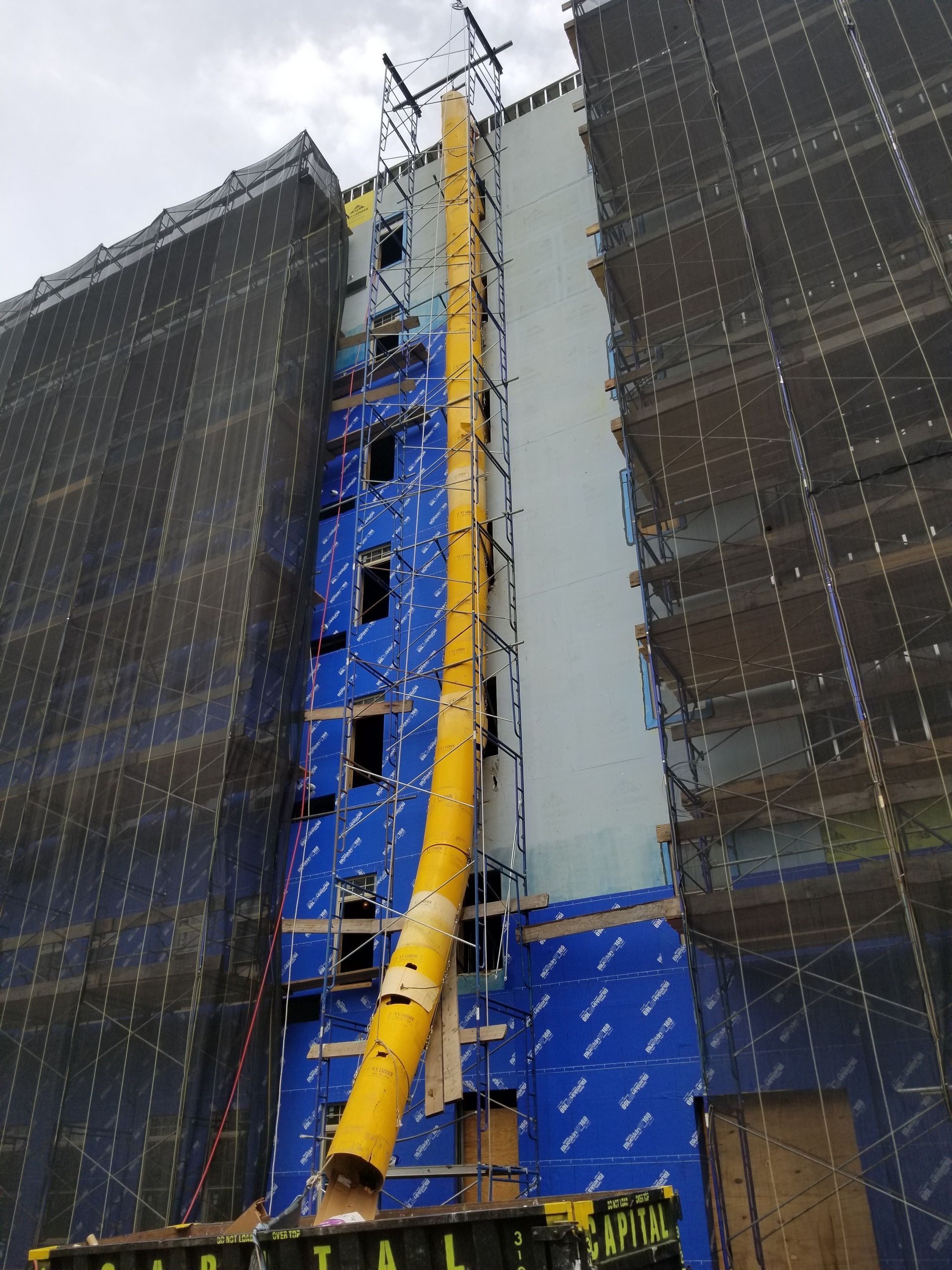 Scaffolding surrounds a multi-story building under construction or repair; blue sky in the background.