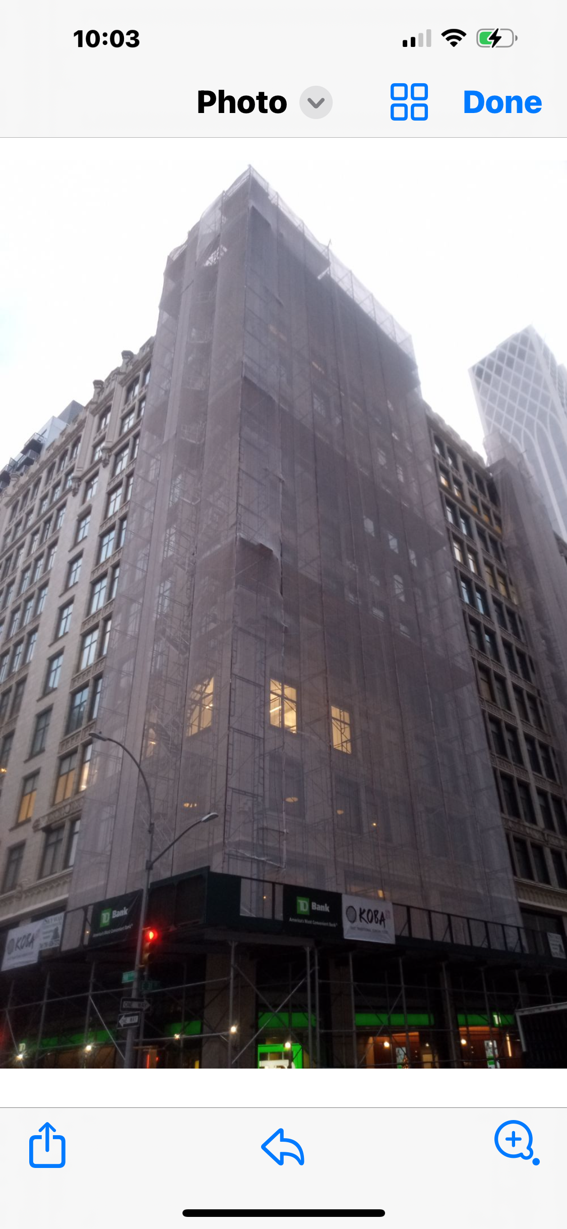 Bamboo scaffolding wraps a glass-walled building under a bright blue sky.