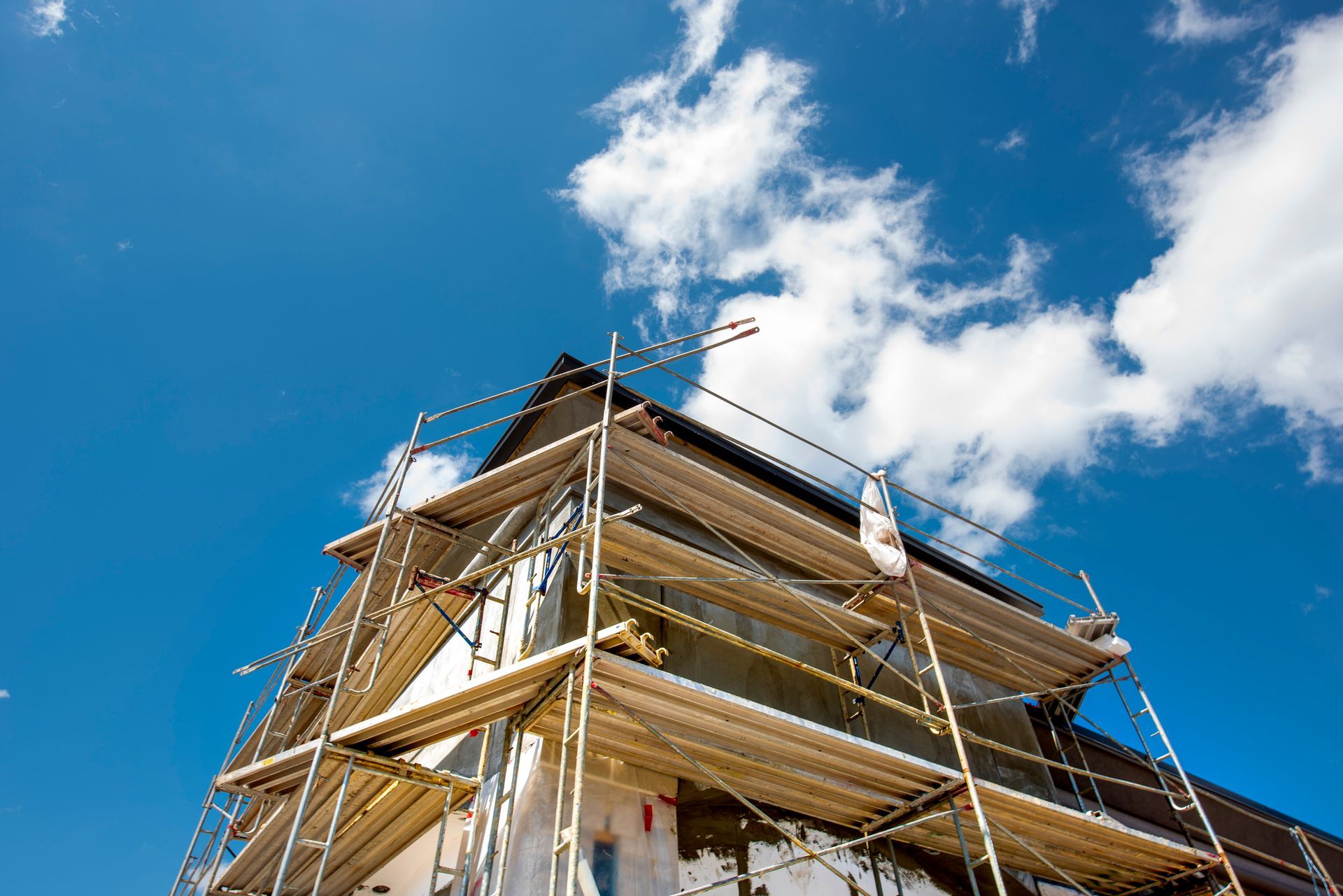 House under construction with scaffolding against a bright blue sky with white clouds.