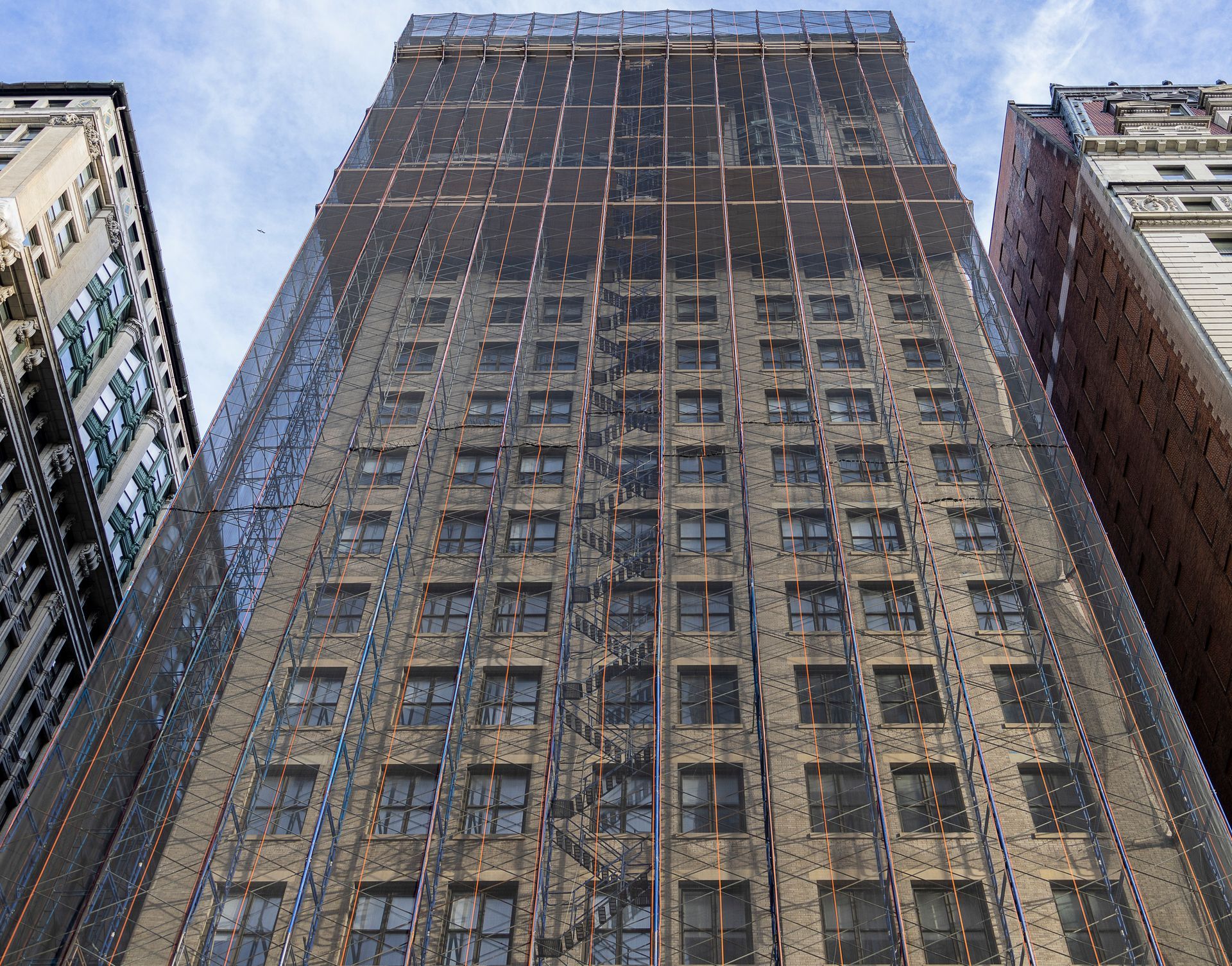 Building under construction with scaffolding and blue safety netting against a clear blue sky.