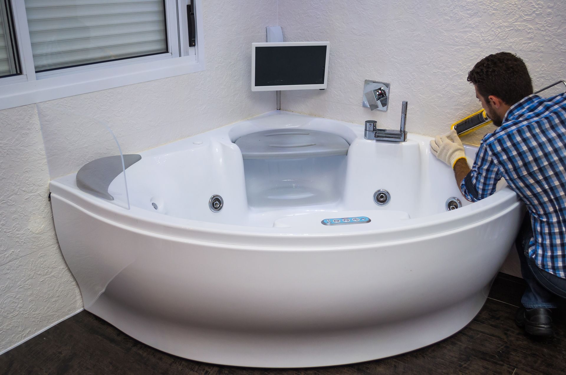Contemporary hot tub installation featuring a built-in TV, with a person applying sealant for a secure setup.
