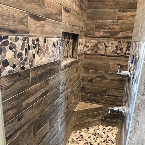 A shower interior featuring brown wood-look wall tiles, a river rock accent border, a built-in niche, and a tiled seat.