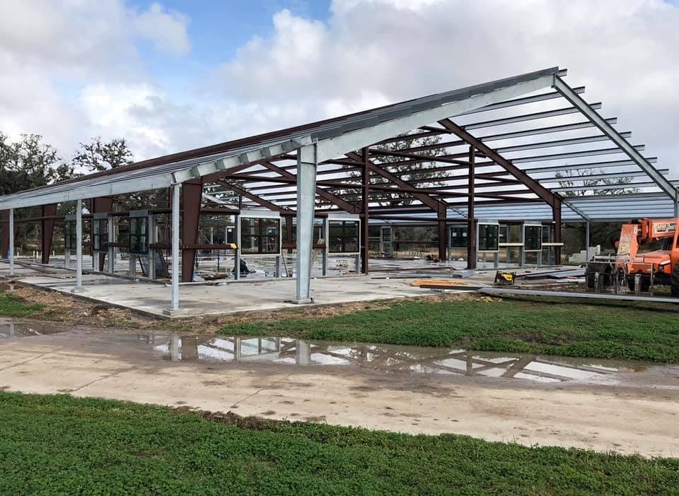 A partially constructed metal-frame building on a concrete foundation under a cloudy sky.